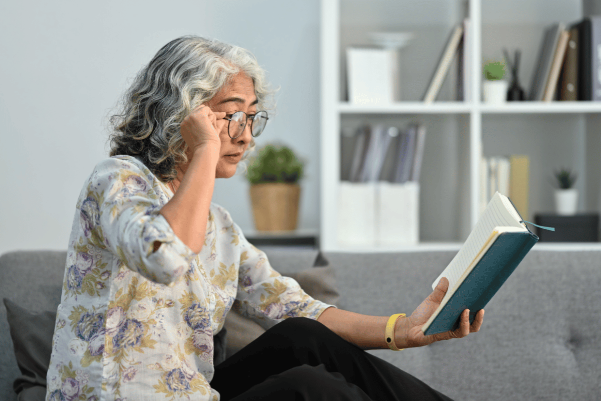 an older woman having trouble seeing a book with her glasses