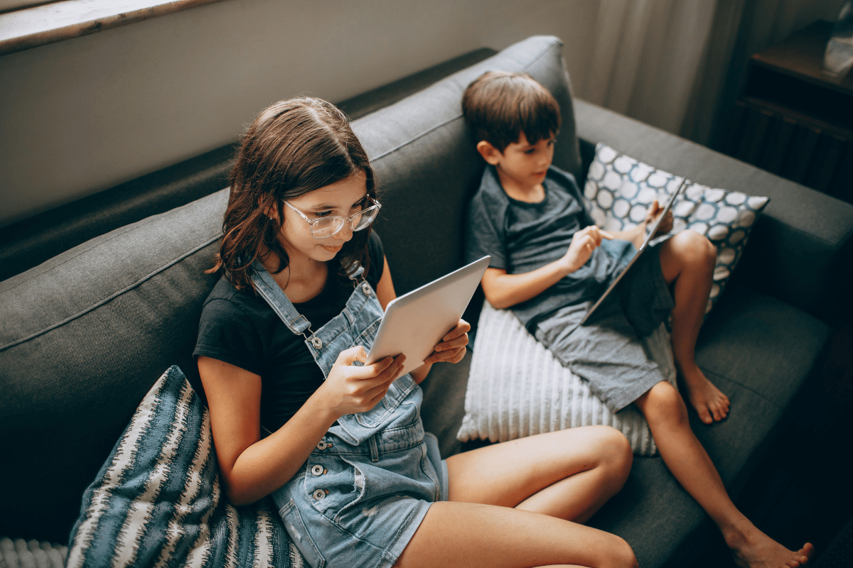 two kids sitting on a couch looking at digital screens