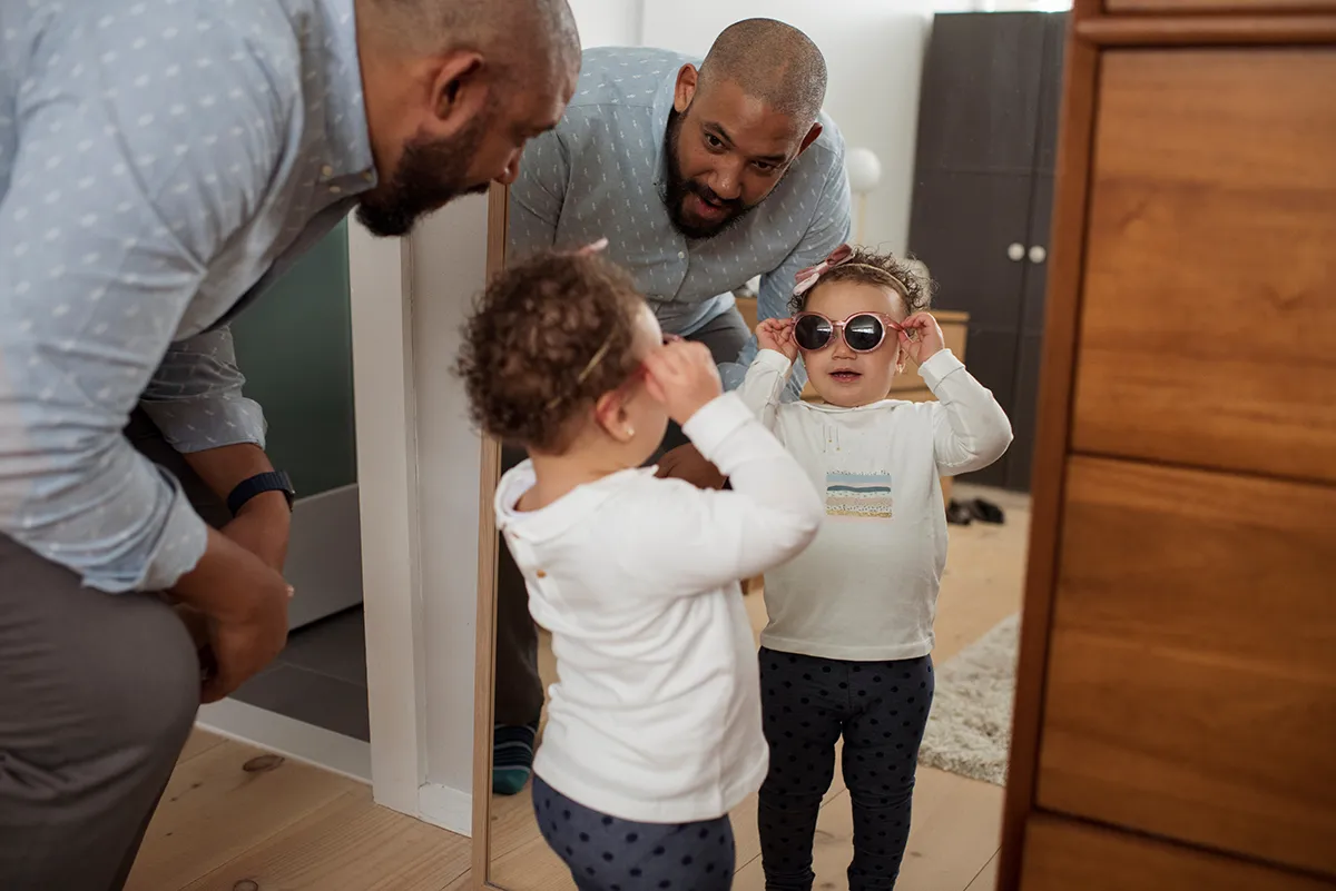 a father standing with his daughter wearing sunglasses while looking in the mirror