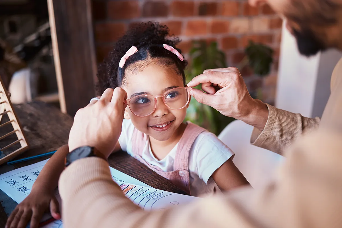 a parent putting glasses on a little girl while she does homework