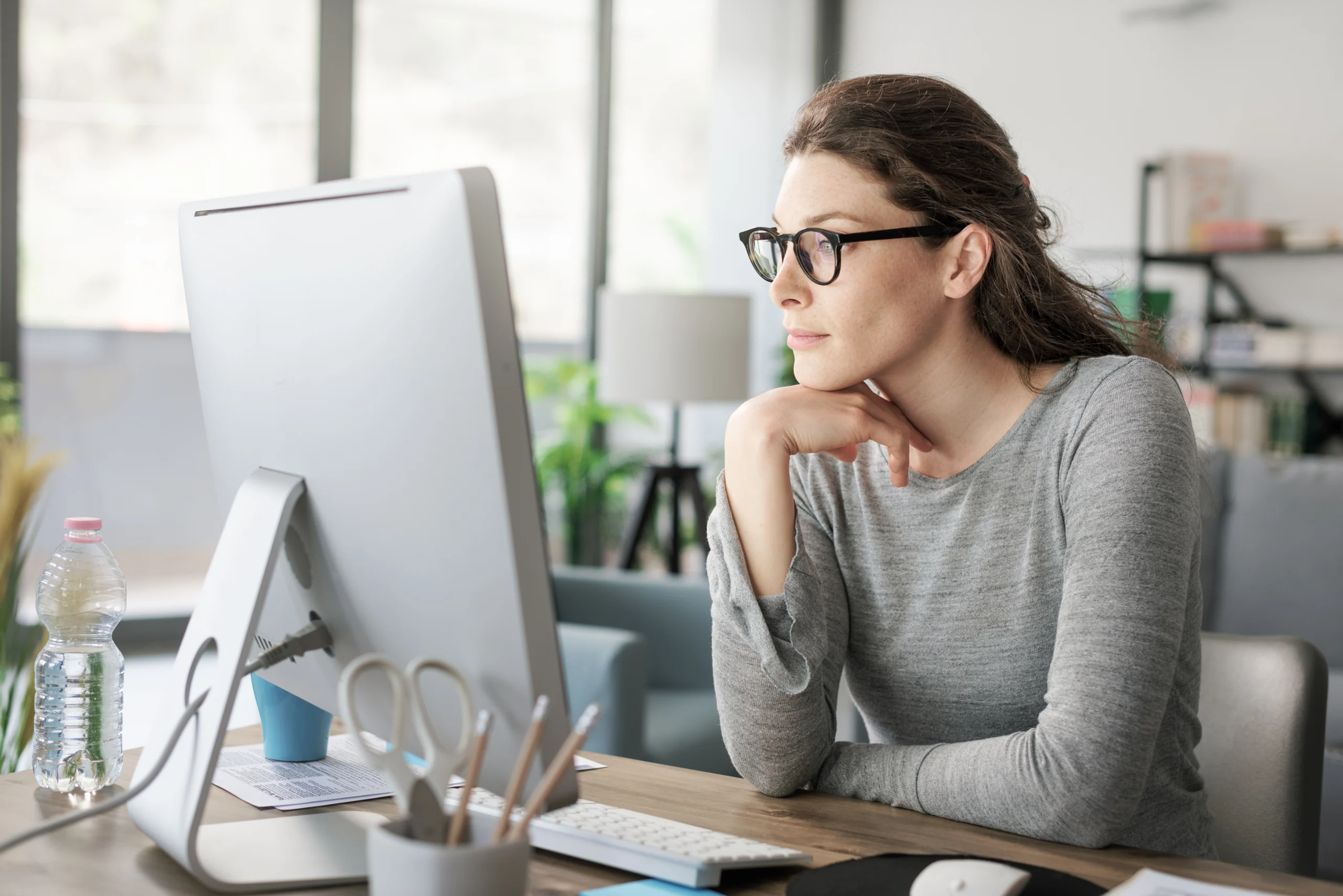 A woman wearing glasses looks peacefully at her computer.